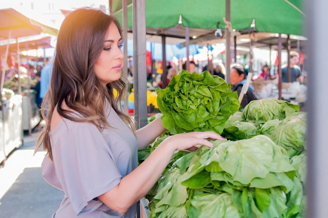 Porträt einer attraktiven jungen Frau, die auf dem grünen Markt grünes Blattgemüse auswählt. Thema: gesunder Lebensmitteleinkauf. Junge Frau kauft auf dem grünen Markt Gemüse.