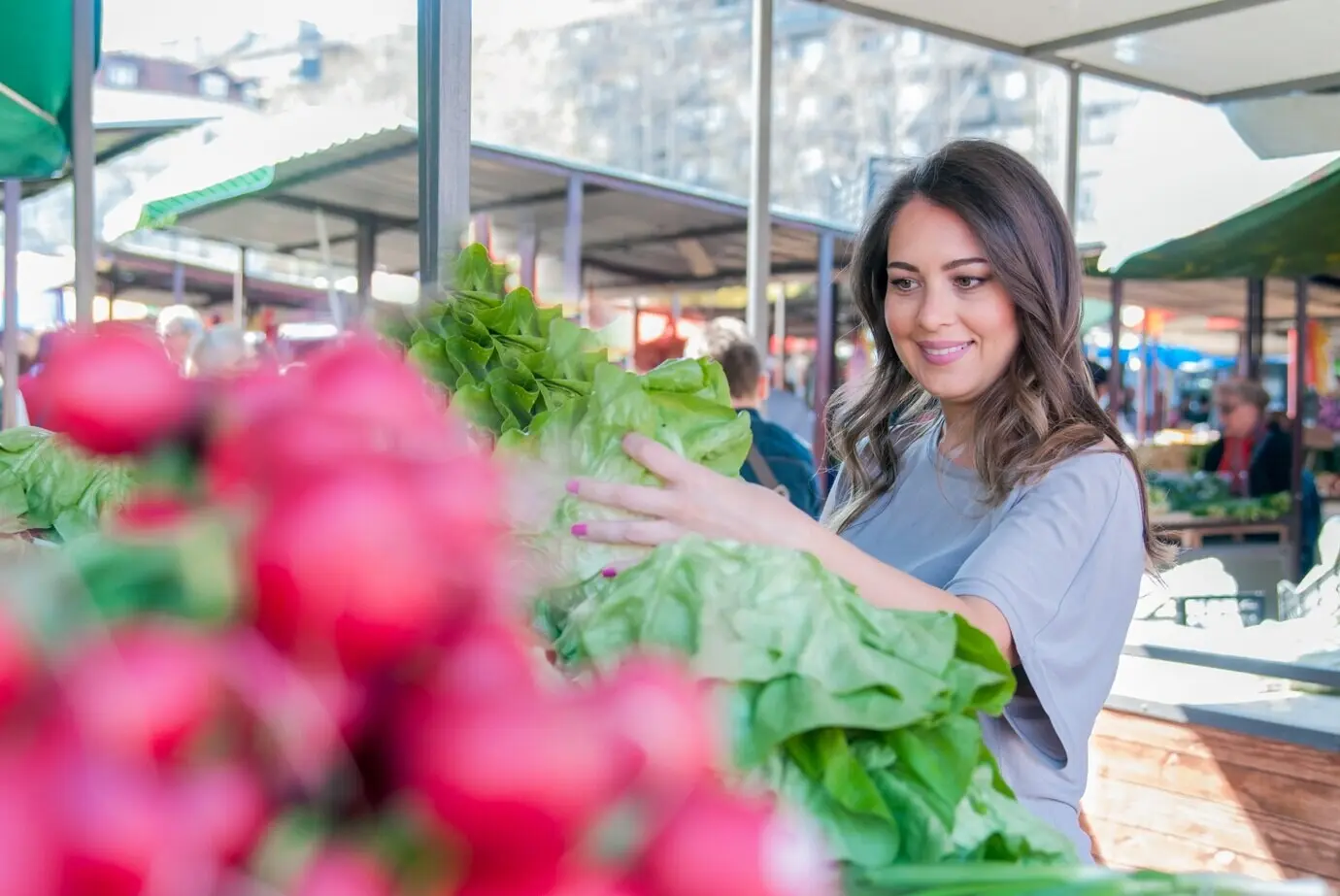 Junge Frau auf dem Markt. Fröhliche junge Brünette, die etwas Gemüse auswählt. Porträt einer schönen jungen Frau, die grünes Blattgemüse aussucht.